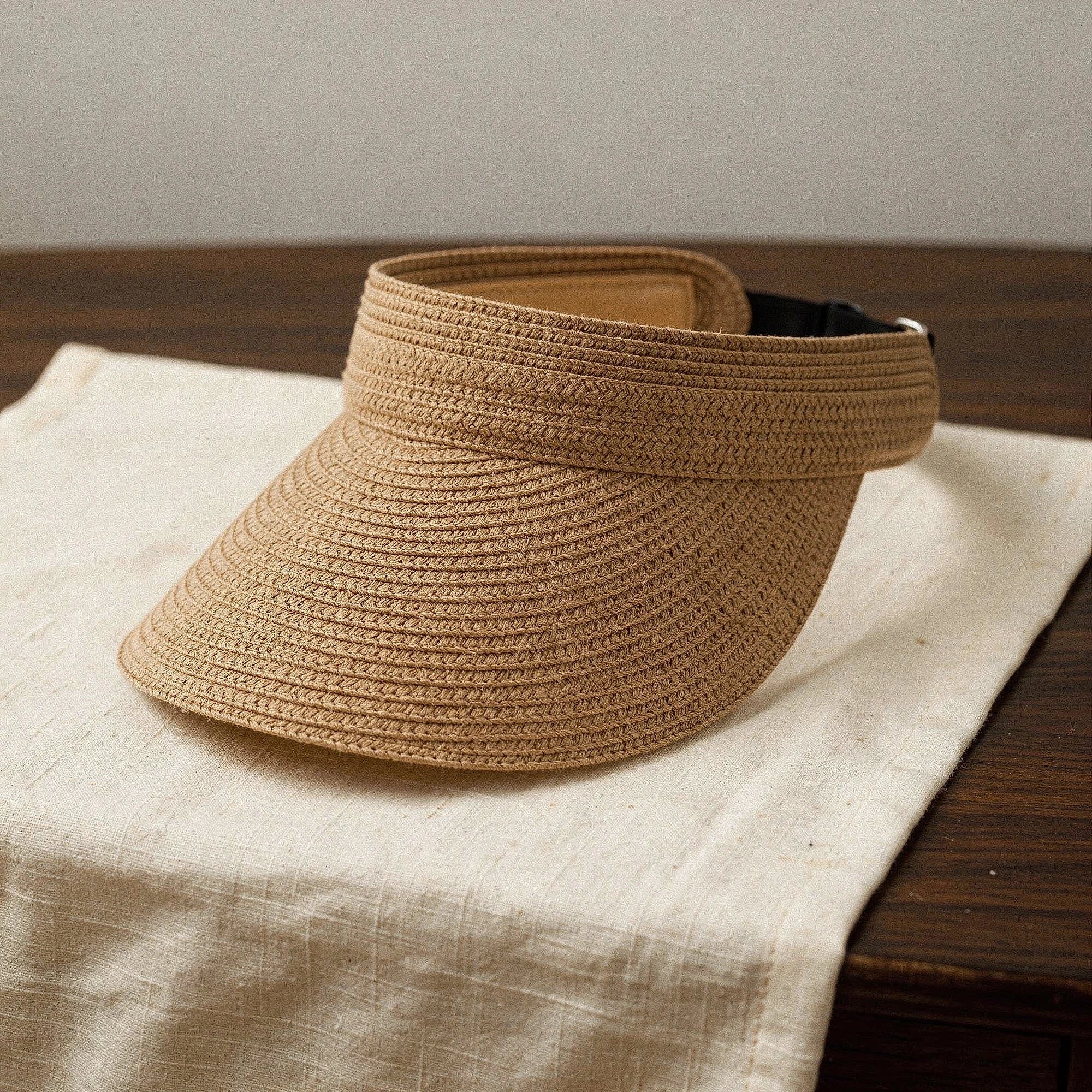 Light beige summer visor hat made of woven straw, featuring a wide brim and decorative ribbon , angled view
