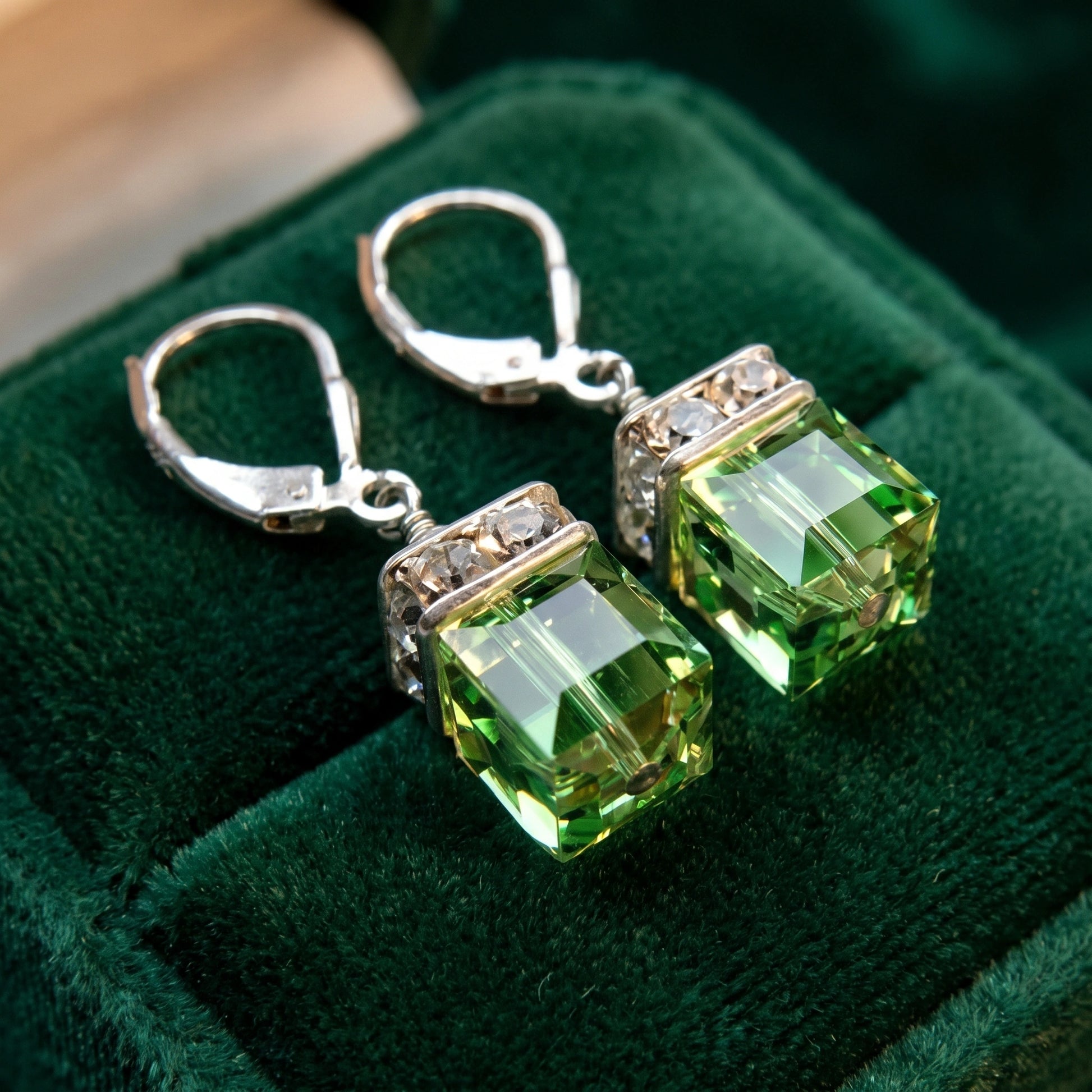 Close up view of Women's Drop Peridot Earrings showing intricate design details and vibrant green gemstones against a soft, neutral background.
