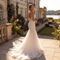 A model showcases the backless wedding dress showing spaghetti straps, displayed against a soft, neutral background that highlights its delicate design and flowing silhouette.