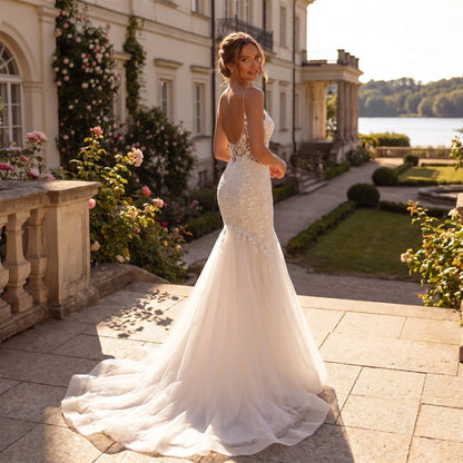 A model showcases the backless wedding dress showing spaghetti straps, displayed against a soft, neutral background that highlights its delicate design and flowing silhouette.