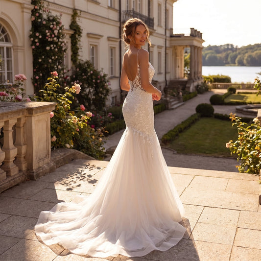 A model showcases the backless wedding dress showing spaghetti straps, displayed against a soft, neutral background that highlights its delicate design and flowing silhouette.