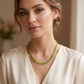 Close up of the Womens Classic Peridot Necklace showing its exquisite craftsmanship and vibrant green stones against a soft, neutral fabric background.