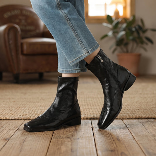 Front view of a model showing women's modern ankle boots in black, styled with a autumn outfit against a neutral background.