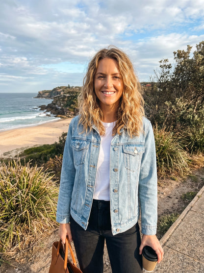 Back view of a model wearing a women's effortless relaxed denim jacket in a light wash, showing stitching details against a neutral background.