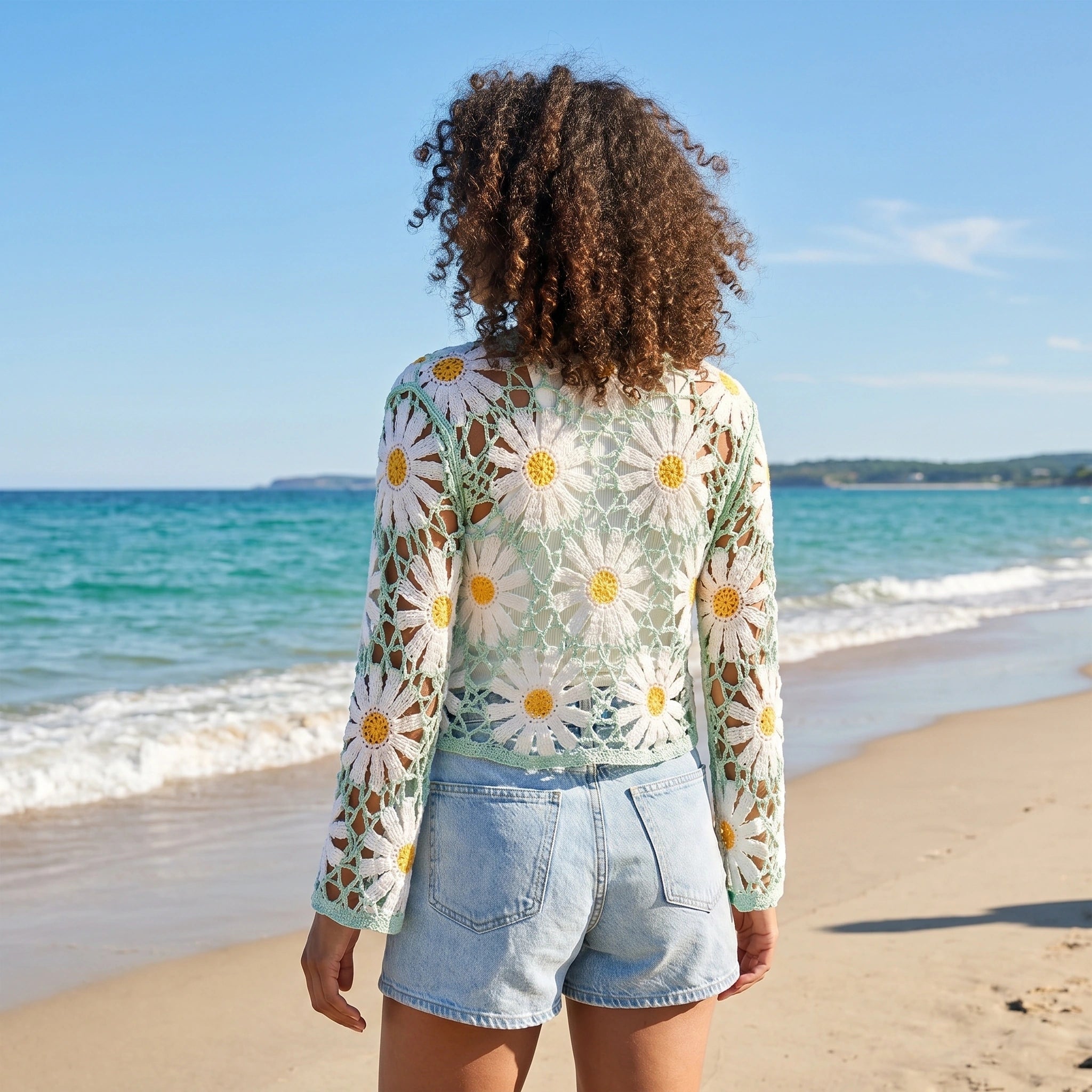 Back view of a model wearing a lightweight sheer boho summer cardigan in Light Green, showing intricate crochet details against a sunlit beach background.