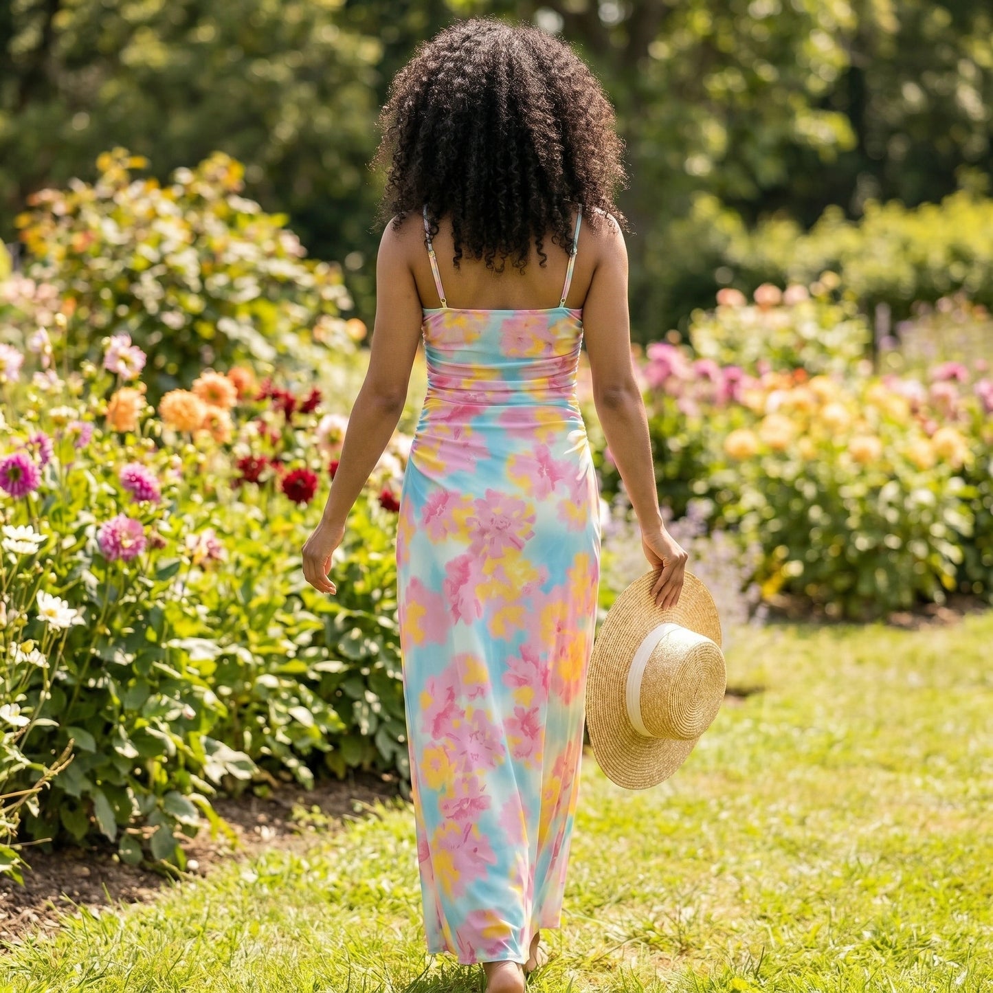 Back view of a model wearing a vibrant floral maxi dress, showing its flowing silhouette and intricate construction details against a soft, neutral background.