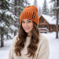 A model showcases the Womens Cozy Knitted Winter Beanie in a winter outfit, showing neutral tones against a soft, blurred outdoor background.