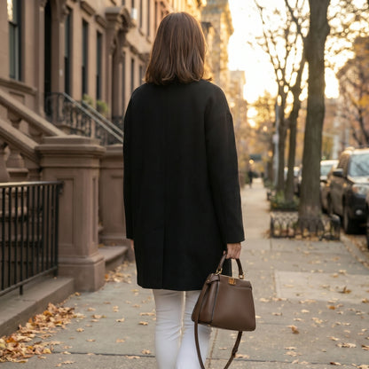 A model showcases a womens polished minimalist winter coat in a sleek black hue, styled with a high waisted outfit against a neutral background.