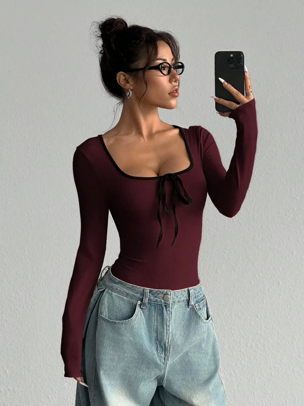 Woman wearing a maroon U neck long sleeve bodysuit with bowknot detail, holding phone — view 15 — view 15