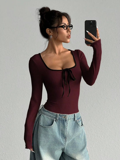 Woman wearing a maroon U neck long sleeve bodysuit with bowknot detail, holding phone — view 15 — view 15