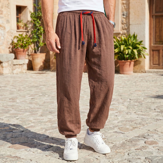 Back view of a model wearing men's relaxed cozy spring linen pants in a light beige color, showing the soft fabric and tailored construction details against a neutral background.