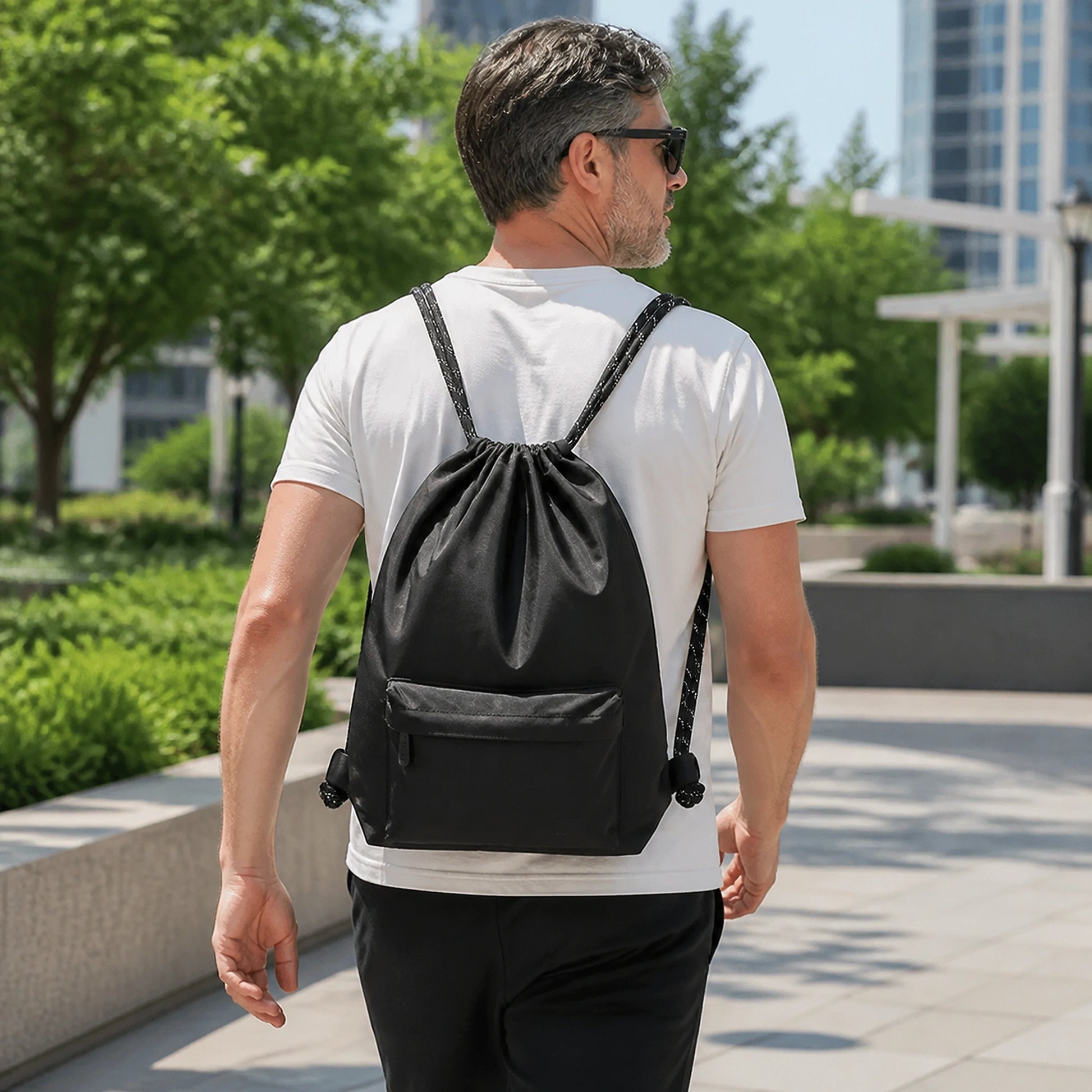 Adult wearing the black drawstring backpack in a city park — view 4