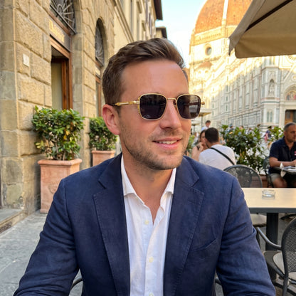 Back view of a model wearing mens sleek summer sunglasses, showing the frame's construction details against a light outdoor background.