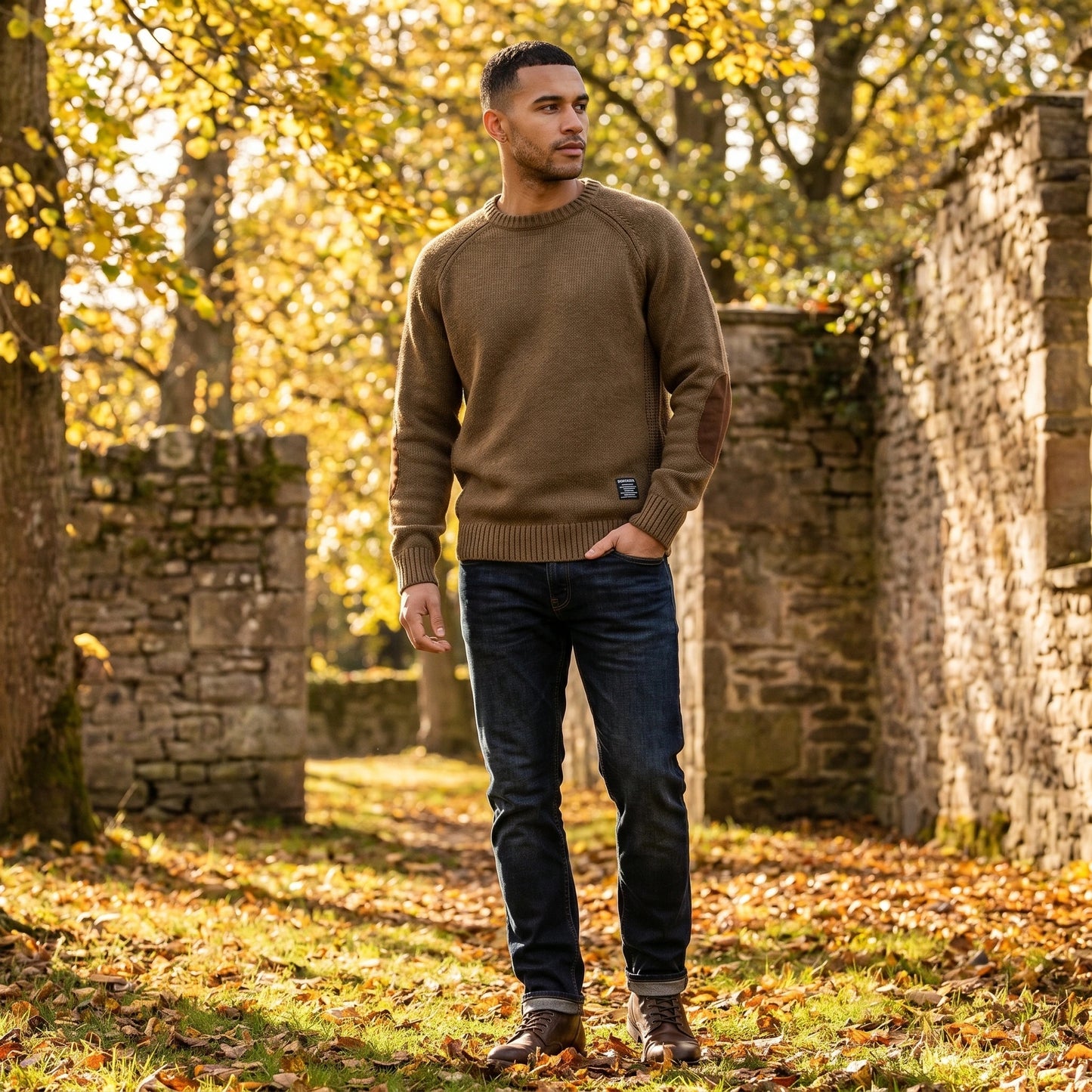 Back view of the Mens Timeless Relaxed Elbow Patch Sweater in a neutral color, showing its construction details and relaxed fit against a soft backdrop.