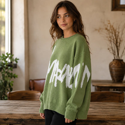 Woman wearing green graffiti jacquard letterman sweater, side view — view 6
