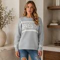 Female model wearing women's gray après ski jacquard letterman sweater, complete front view