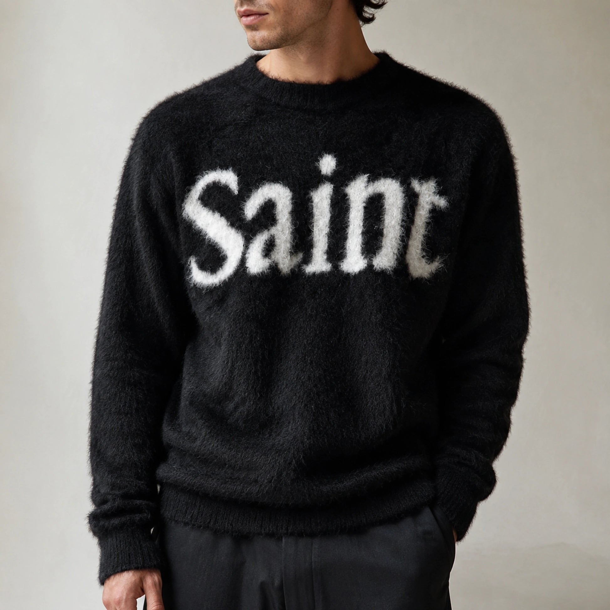 Male model wearing black fuzzy script letterman sweater, close up neckline and knit detail — view 4