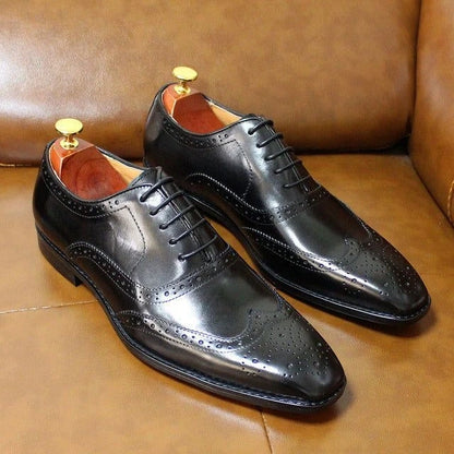 Black leather oxford loafers with brogue detailing on a brown surface — view 2 — view 3
