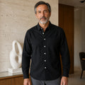 Mature man wearing Black slim fit long sleeve Oxford shirt, full front view with point collar, white buttons, chest pocket