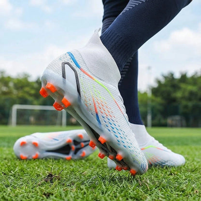 White high cut soccer cleats with orange studs and colorful accents on grass field